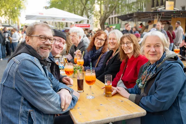 Gäste lächeln an einem Holztisch mit Spritz, Wein und Bier