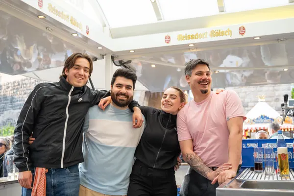 Vier junge Leute lachen an einem Bierstand