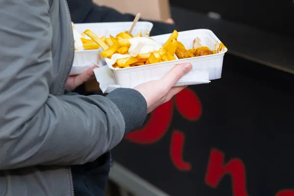 Zwei Schalen Pommes und Currywurst, von einer Hand gehalten