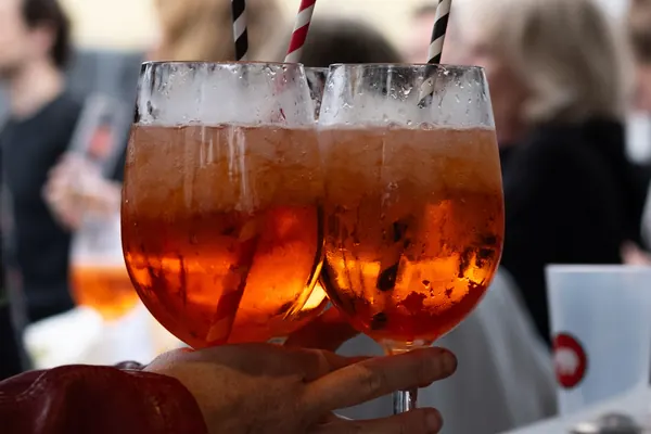 Aperol-Spritz-Gläser mit Strohhalmen in einer Hand