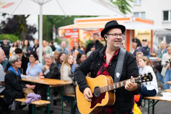 Ein Musiker mit Hut spielt Gitarre vor Publikum an Biertischen