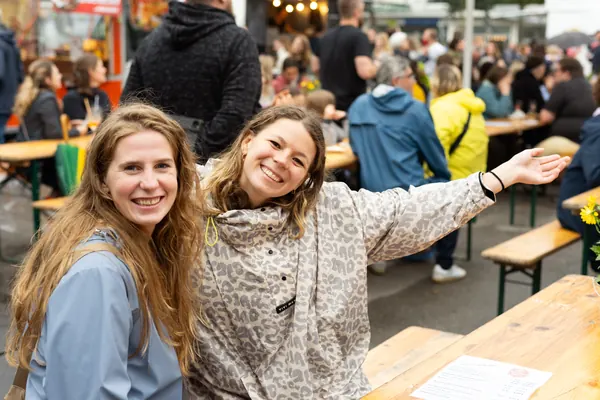 Zwei Frauen lachen in die Kamera, dahinter Biertische
