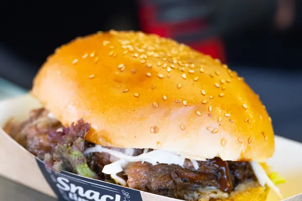 Ein Burger mit Sesambrötchen in einer Pappschale
