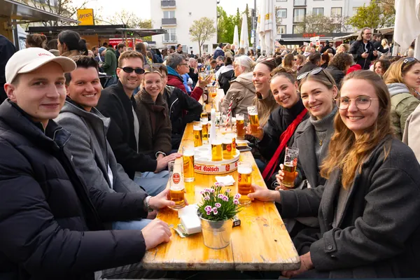 Gäste lächeln an einem langen Holztisch mit Kölsch