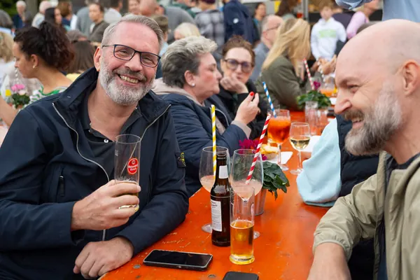 Ein Mann mit Bier lacht an einem Tisch, daneben ein weiterer Gast