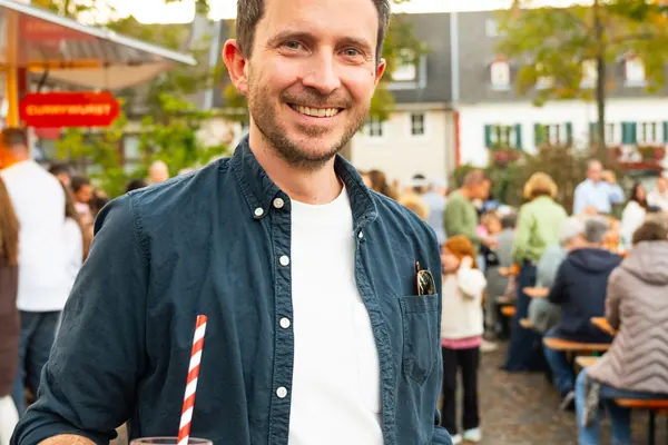 Ein Mann lächelt in die Kamera, in der Hand einen Spritz und eine Pizza