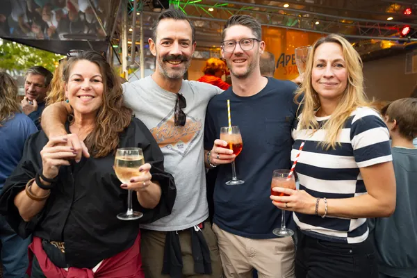 Vier Freunde mit Wein und Spritz unter bunten Lichtern
