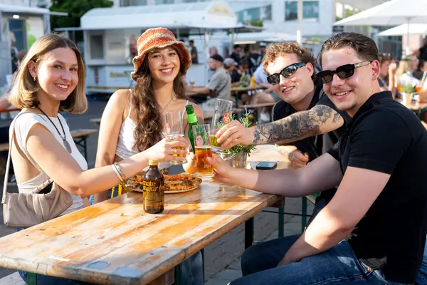 Vier junge Leute stoßen an einem Biertisch an