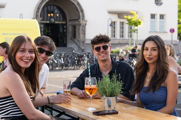 Vier Freunde mit Spritz an einem Tisch vor einem Gebäude mit Rundbogen