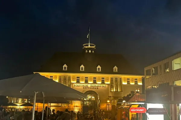Das beleuchtete Neptunbad bei Nacht, davor Schirme und Imbissstände